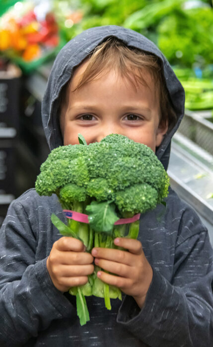A little boy holding a head of broccoli up to his face