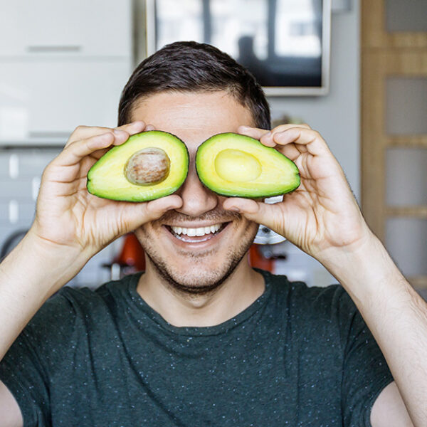 A smiling man holds a sliced avocado up to his eyes