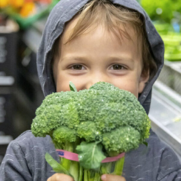 A young boy holds a head of broccoli up to his face